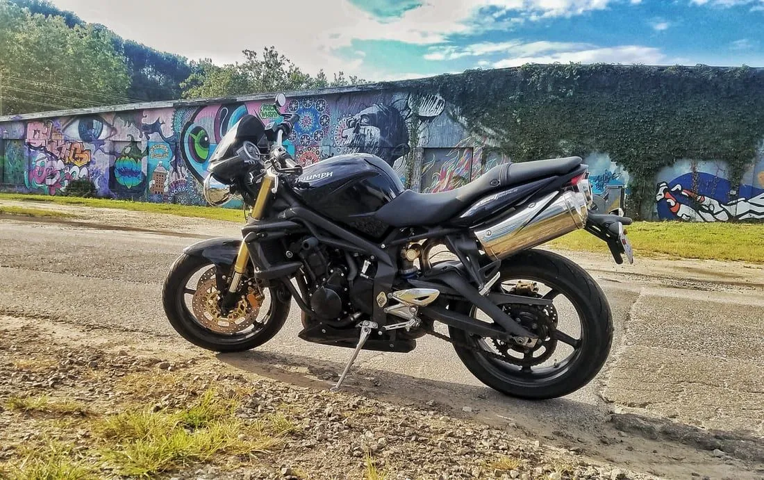 A black Triumph naked motorcycle parked beside a graffiti wall in Western North Carolina
